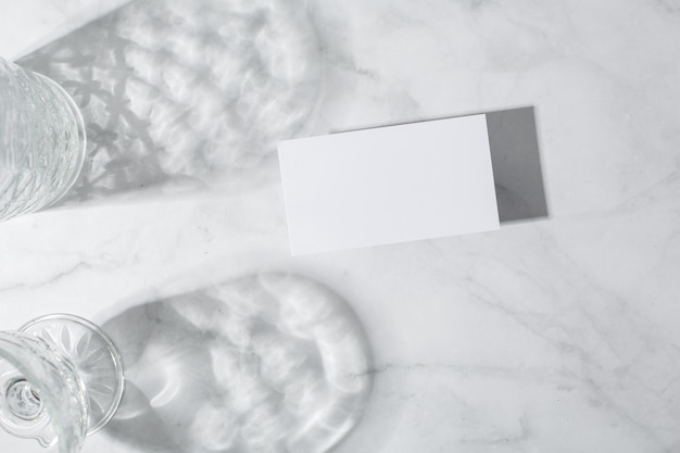 Still life scene with glasses on marble background in sunlight and blank business greeting card invi