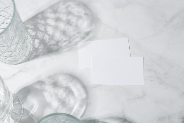 Still life scene with glasses on marble background in sunlight and blank business greeting card invi