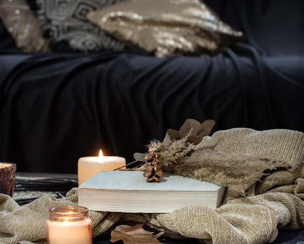 Still life on the table with candles, sweater book and autumn leaves. Cozy living room, home interior decor.