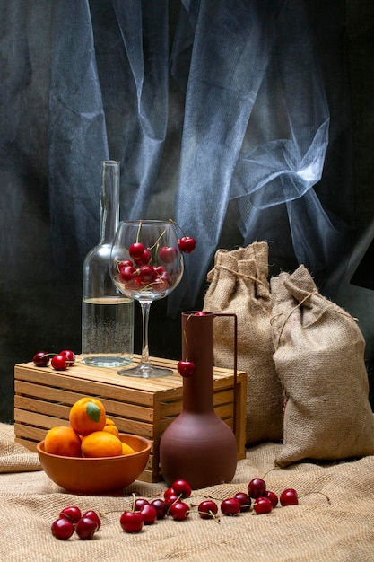 Still life with bags ripe cherries in a glass and a bottle