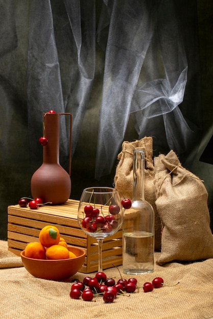 Still life with bags ripe cherries in a glass and a bottle