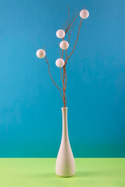 Still life with a branch and white balls in a white vase on a colored background