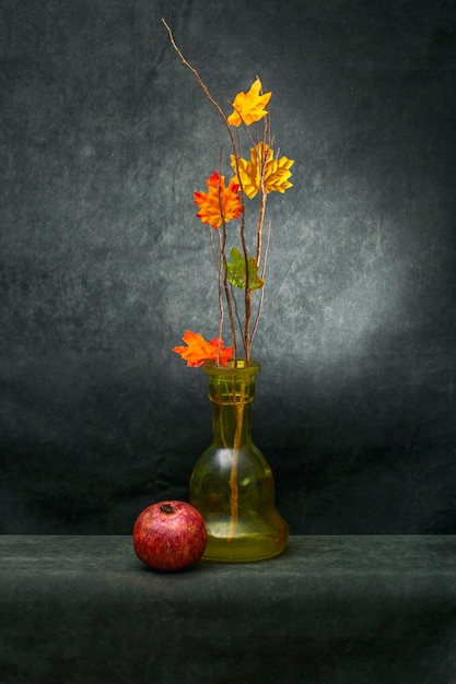 Still life with a branch with autumn leaves and ripe pomegranate fruit