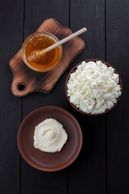 Still life with cheese and honey on a wooden black background Curd mass and cottage cheese on a clay plate on a wooden board Closeup View from above