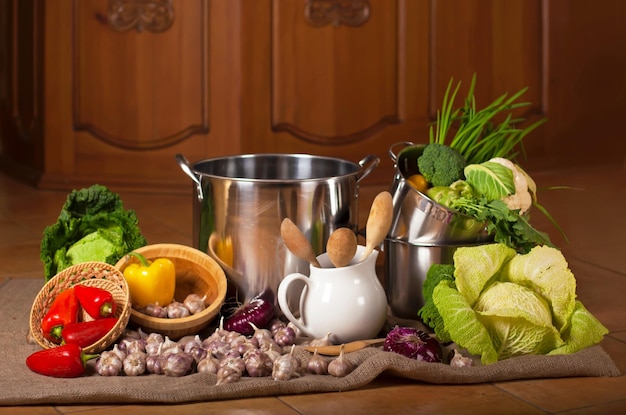 Still life with crockery and a variety of fresh organic vegetables Food and fresh raw vegetables arranged around the stainless steel pan