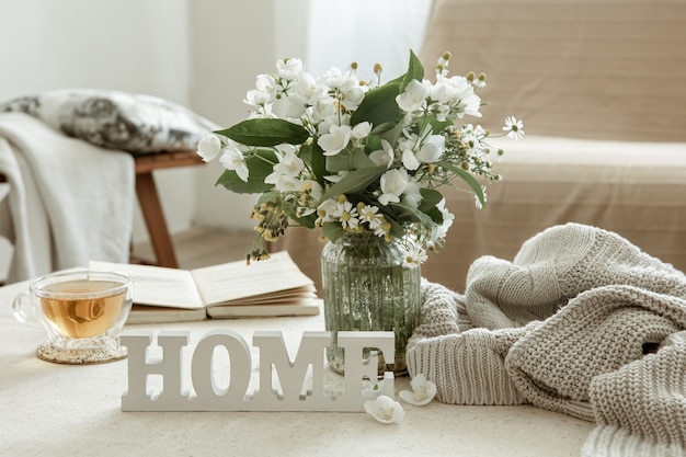 Still life with a cup of herbal tea, a bouquet of flowers, a book and a wooden decorative word home.