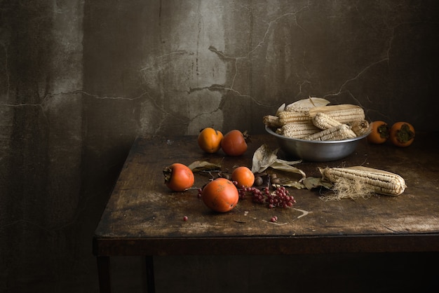 Still life with fruit and corn in an aluminum bowl on a wooden old table