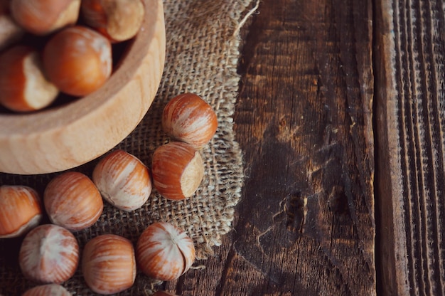 Still life with hazelnut kernels and whole hazelnuts on a rustic old wooden table with a spoon and a bowl of wood with place for your text