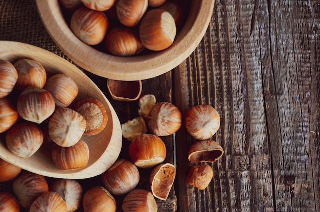 Still life with hazelnut kernels and whole hazelnuts on a rustic old wooden table with a spoon and a bowl of wood with place for your text