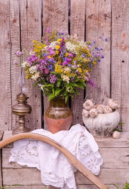 Still life with a multicolored bouquet of wild flowers in a jug on a wooden background in a rustic style