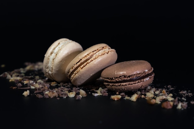 Still life with three macaron cookies on nut crumbs isolated against dark background