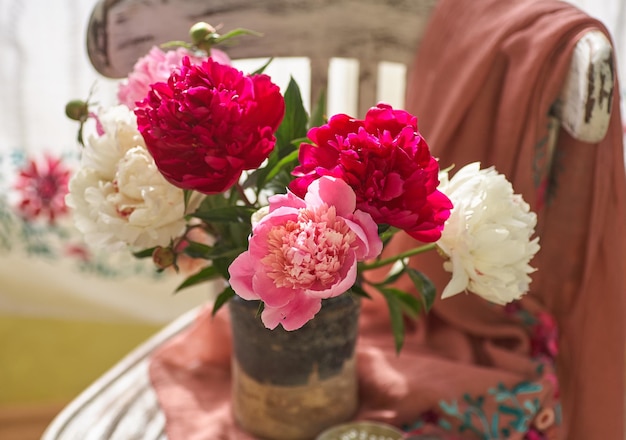 Still life with white and pink peonies in a old ceramic vase on vintaje chair