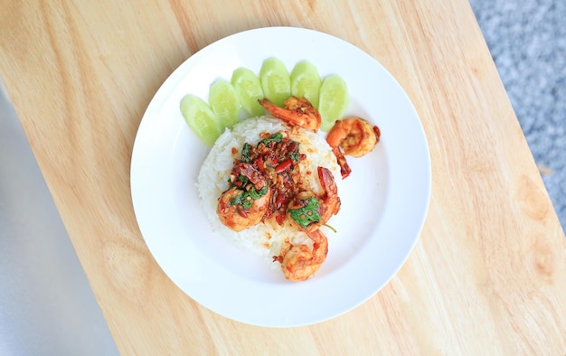 Stir fried holy basil leaves with shrimps prawns topped on jasmine rice in plate on wood table Top view