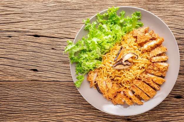 Stir fried instant noodles with Japanese deep fried pork cutlet or Tonkatsu, lettuce and Shiitake mushroom on rustic wood texture background with copy space for text, top view