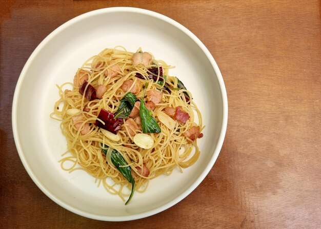 Stir fried spaghetti with dried chili and crispy bacon in white plate on wooden background