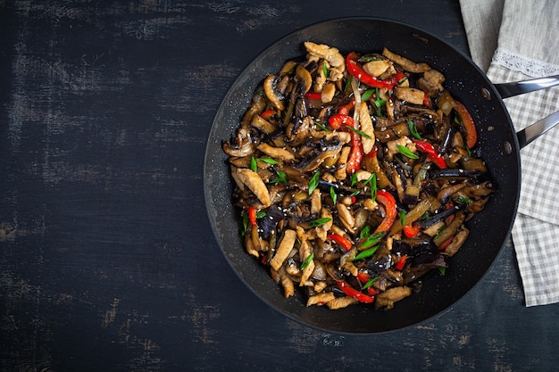 Stir fry with chicken eggplant and pepper in wok pan on dark background