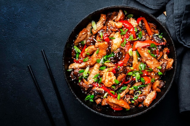 Stir fry with turkey fillet paprika mushrooms green chives and sesame seeds in frying pan Asian cuisine dish Black stone kitchen table background top view