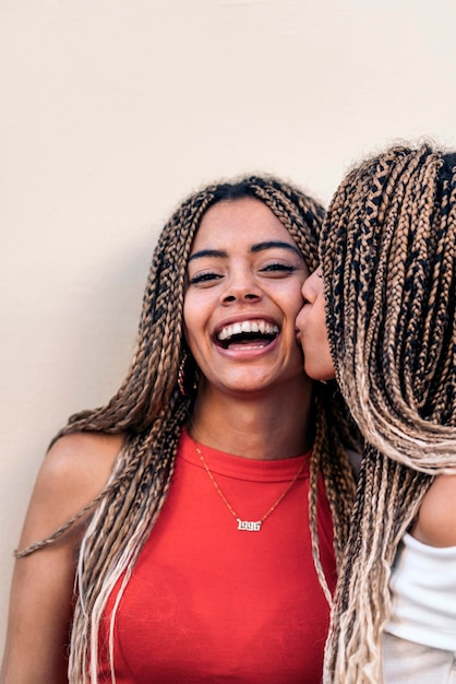 Stock photo of attractive african american sisters with cool braids having fun and kissing.