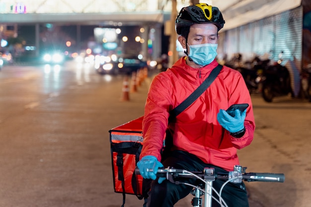 Stock photo of a food deliveryman in red uniform carrying a food delivery box to deliver for customer for order during COVID-19 pandemic and  lockdown in the city at night time in Thailand.