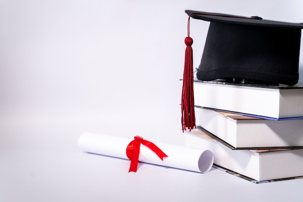 Stock photo of a graduation cap mortar board and diploma certificate isolated on white background with negative copy space to add text. Graduation hat with diploma on table against white background