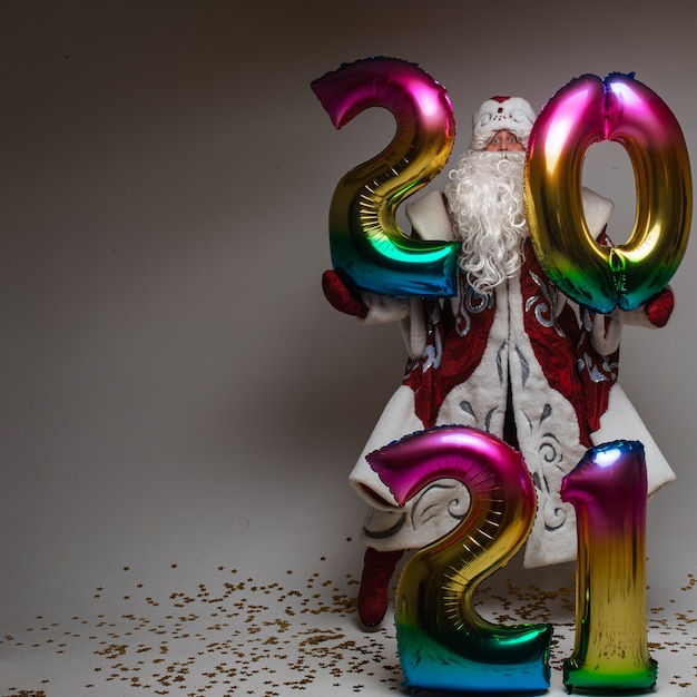 Stock photo of jolly Father Frost in festive clothing with long white beard outstretching his arms and smiling at camera under flying golden confetti. Isolated on grey background.