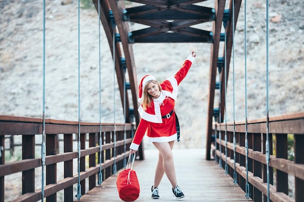 Stock photo of Mama Noel playing happily with the red bag of gifts on a wooden bridge Christmas time