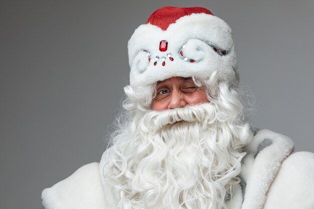 Photo stock photo of smiling happy santa in traditional hat with rhinestones and long white beard looking at camera. cutout on red background. happiness concept.