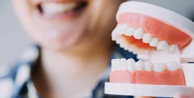 Stomatology concept partial portrait of girl with strong white teeth looking at camera and smiling fingers near face Closeup of young woman at dentist's studio indoors