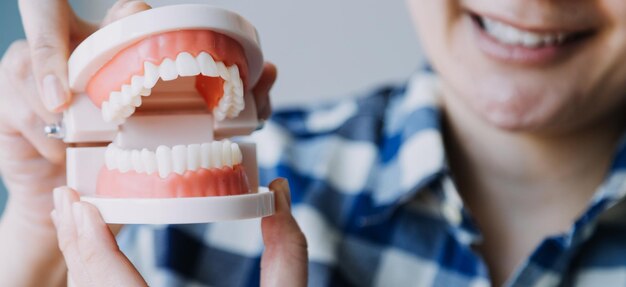 Stomatology concept partial portrait of girl with strong white teeth looking at camera and smiling fingers near face Closeup of young woman at dentist's studio indoors