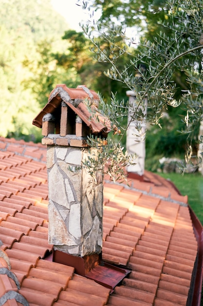 Stone chimney on a tiled roof against a background of green tree branch