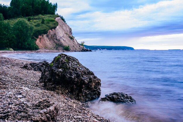 Stone on the riverbank and cliff with birch woodland on background