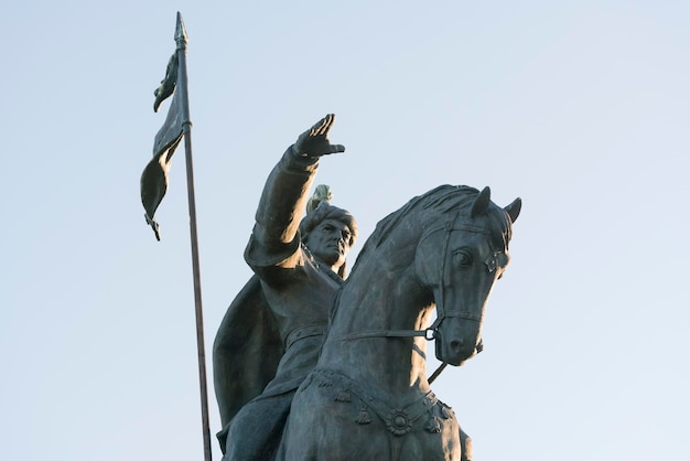 Stone sculpture of a man on horseback with flag on a sky background