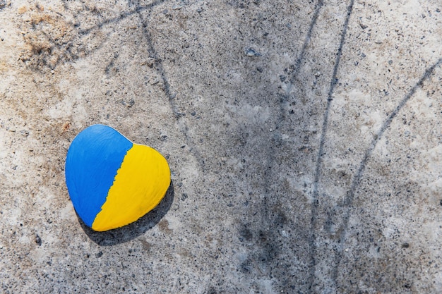 Stone in shape of heart painted with Ukrainian flag lies on the ground concrete