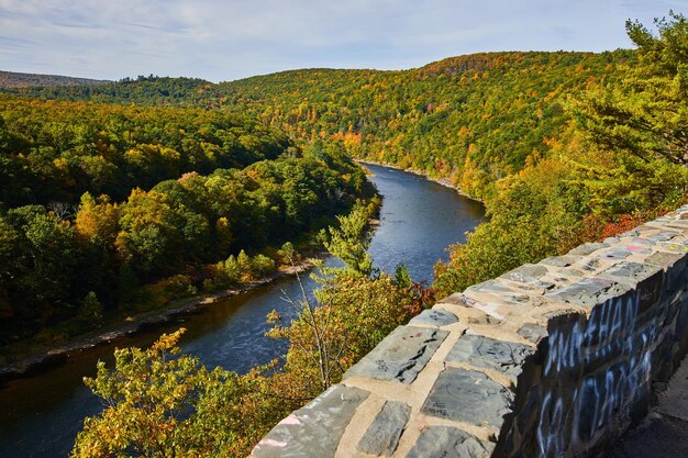 Stone wall along overlook above Delaware River going through early fall forest