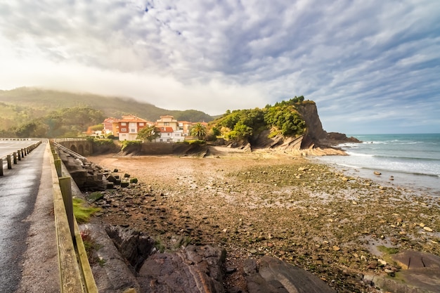 Stony beach with seaside houses, cliffs and dramatic sky with cumulus clouds. Vizcaya, Basque country. Spain