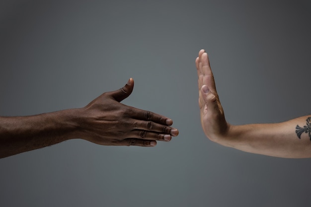 Stop shaming. Racial tolerance. Respect social unity. African and caucasian hands gesturing on gray studio background. Human rights, friendship, intenational unity concept. Interracial unity.