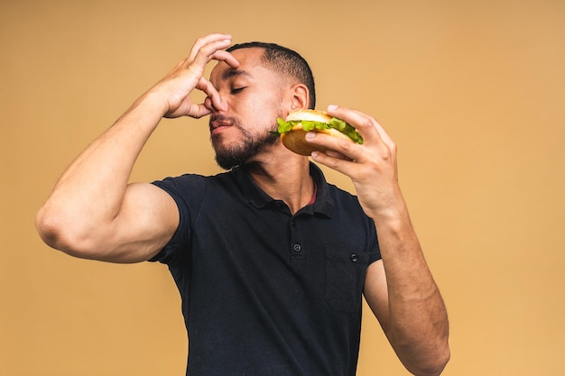 Stop sign bad smell Young african american black man eating hamburger isolated over beige background Diet concept