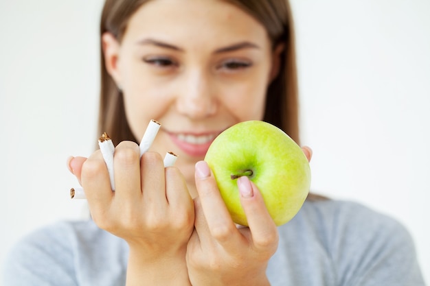 Stop smoking, woman holding broken cigarettes and green apple in hands.