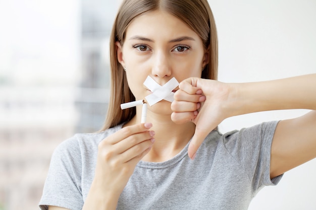 Stop smoking, a woman with a sealed mouth holding a broken cigarette