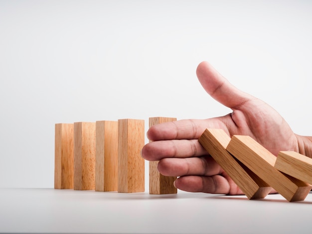 Photo stopping the domino effect. business crisis management. close-up hand interfering collapsing wooden dominoes on white background. business strategy and successful intervention. risk protection.