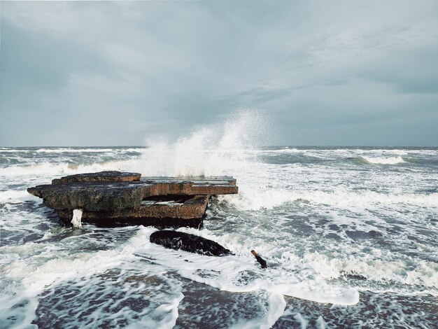 Storm waves crashes against rocks of sea coast on cloudy sky background