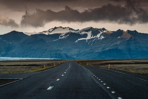 Straight asphalt road with storm over mountain on gloomy day in Iceland