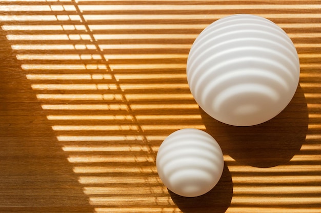 Straight and curved shadows on spherical surface of white frosted glass balls and wooden plane