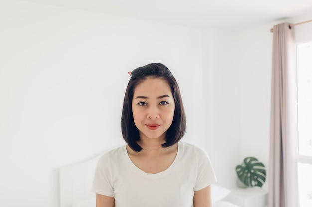 Straight portrait of woman standing in white bedroom.