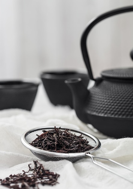 Strainer infuser with loose black tea on light cloth with iron teapot and cups