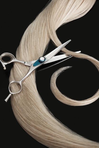 A strand of blond hair with scissors on a black background Closeup