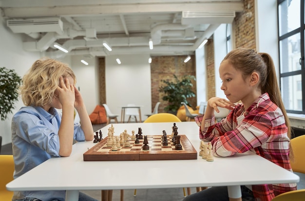 Strategy concentrated boy and girl developing chess strategy playing board game sitting together at