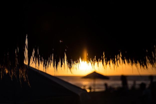 Straw beach roof in the cafe with blurred people on beautiful tropical sunset