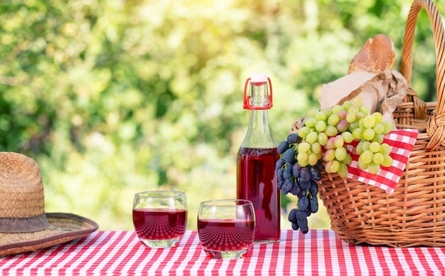 Straw hat, basket with grapes and juice on red checkered tablecloth