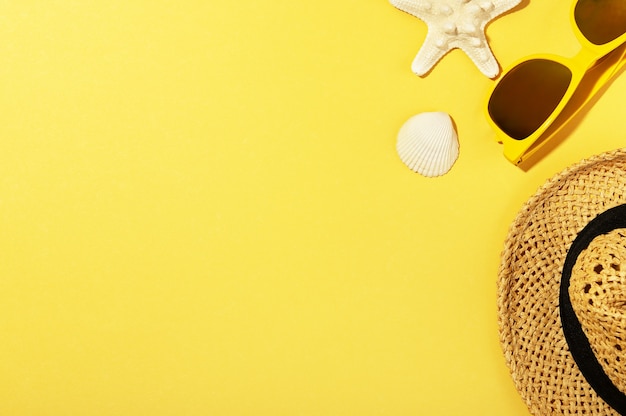 Straw hat, sunglasses, shell and starfish isolated on yellow background. Blank copy space in left side. Summer backdrop. Summer-time and travelling concept.